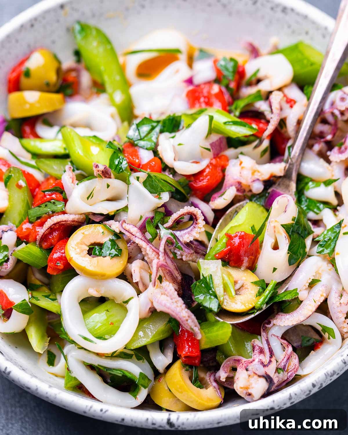 Zesty Italian Calamari Salad 2 White bowl with Italian calamari salad and serving spoon on blue background.