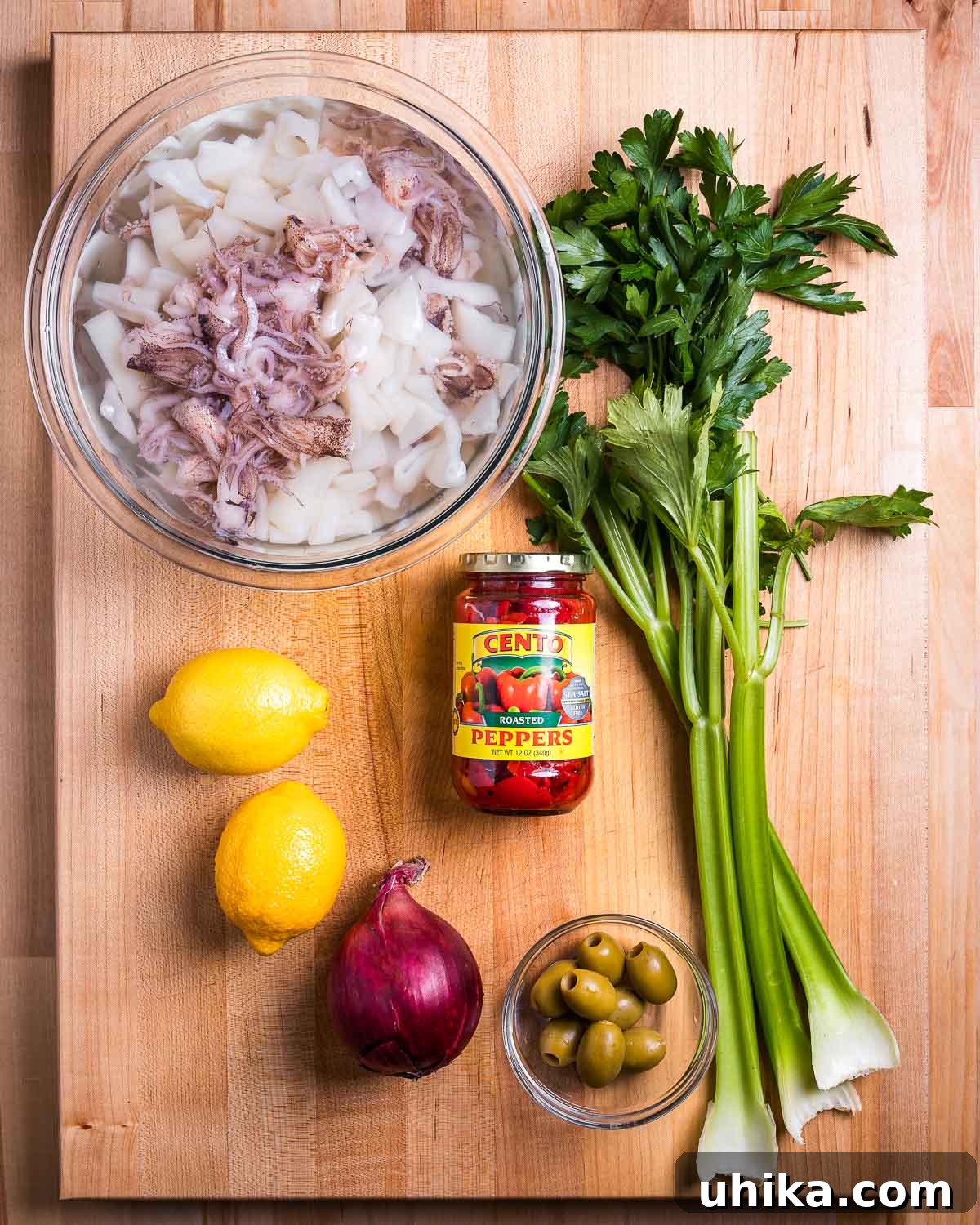 Zesty Italian Calamari Salad 3 Ingredients shown: bowl of calamari, celery, parsley, lemons, roasted red peppers, red onion, and olives.
