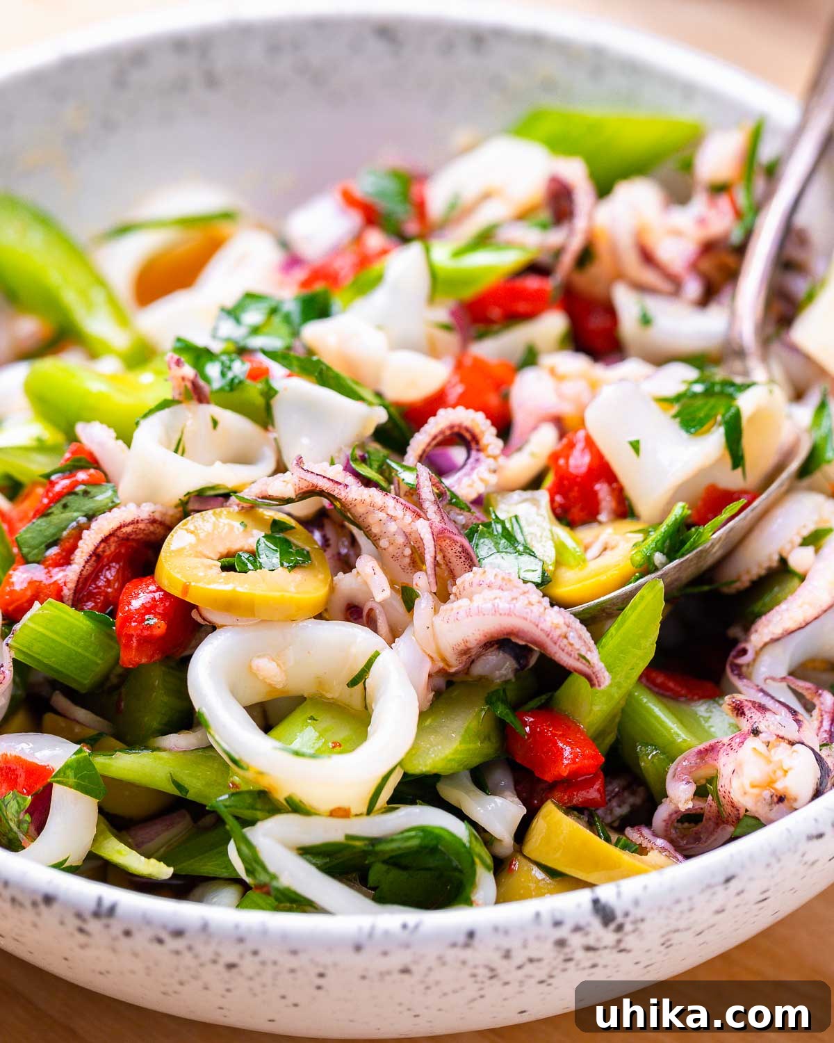 Zesty Italian Calamari Salad 9 White bowl with Italian calamari salad and serving spoon.