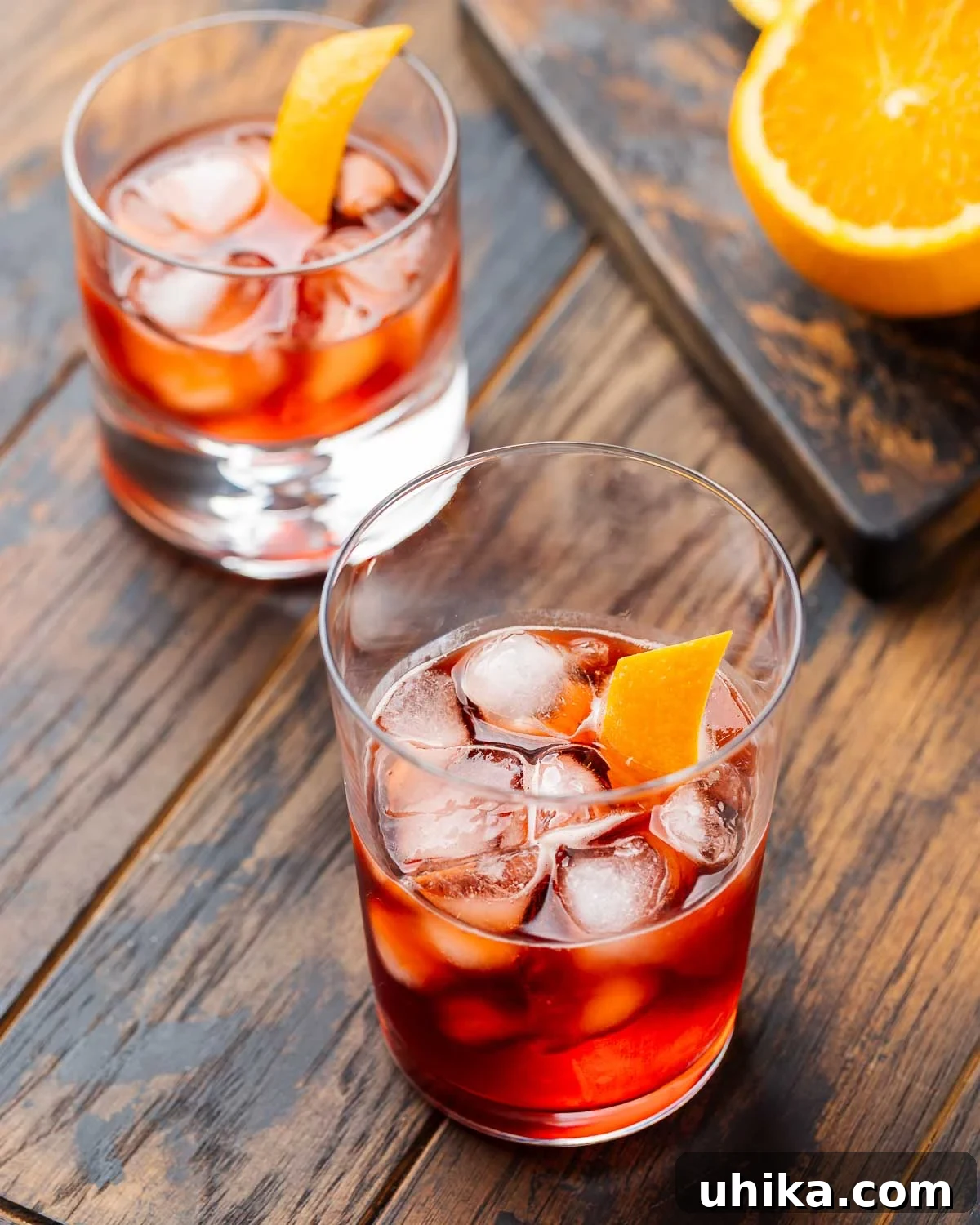 Timeless Negroni 2 Two Negronis on a wooden board with a cut orange in the background.