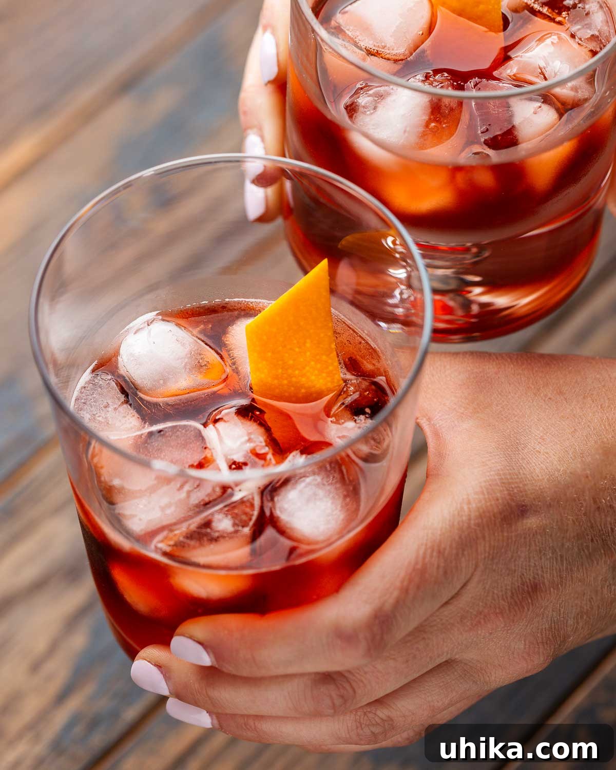 Timeless Negroni 4 Hands holding two Negroni cocktails.