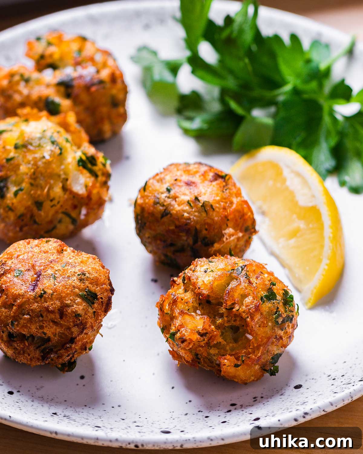 Mediterranean Salt Cod Fritters 2 Baccala fritters served on a white plate with a lemon wedge and parsley garnish, ready to eat.