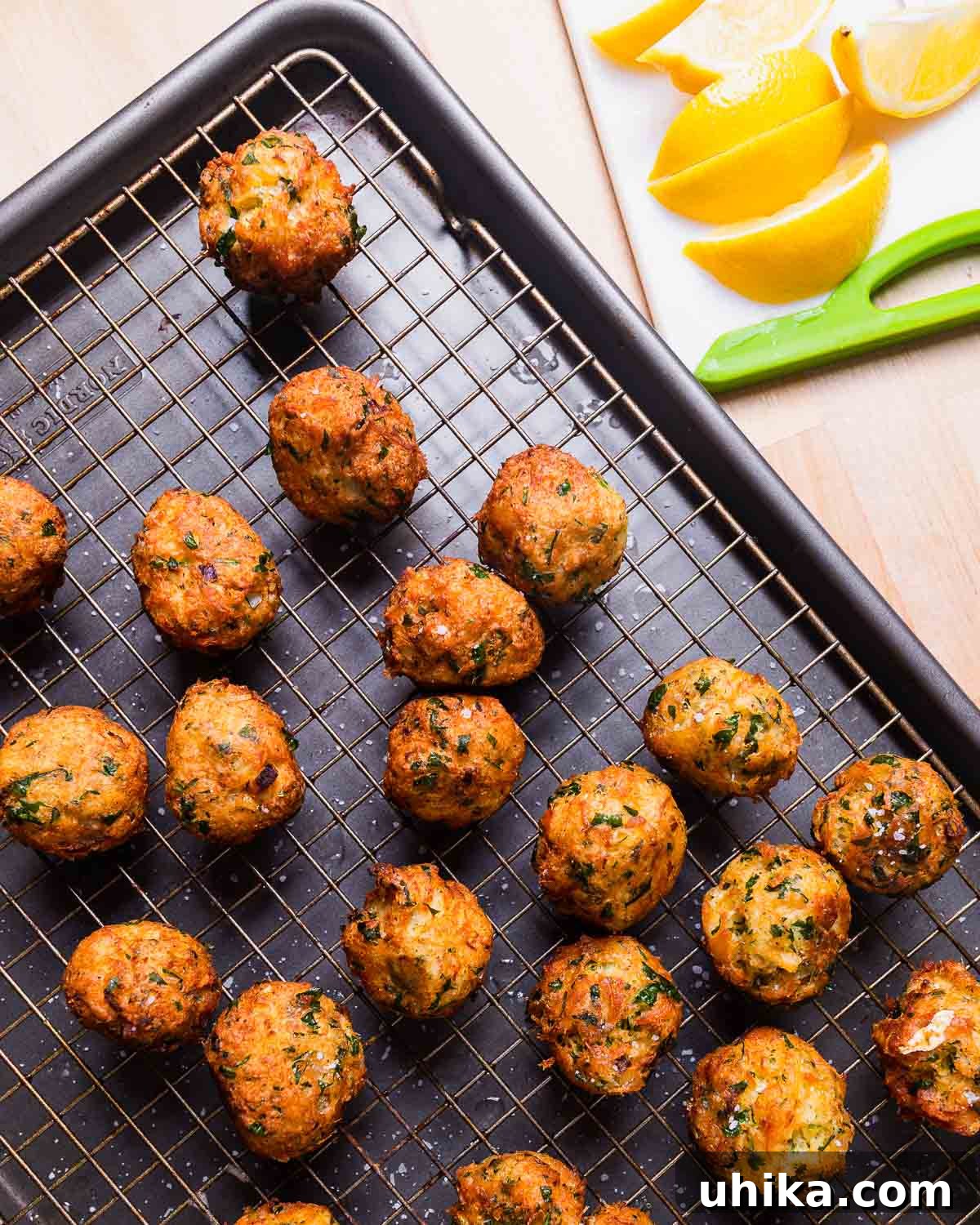 Mediterranean Salt Cod Fritters 9 Freshly fried baccala balls resting on a wire rack, with lemon wedges arranged neatly on the side.