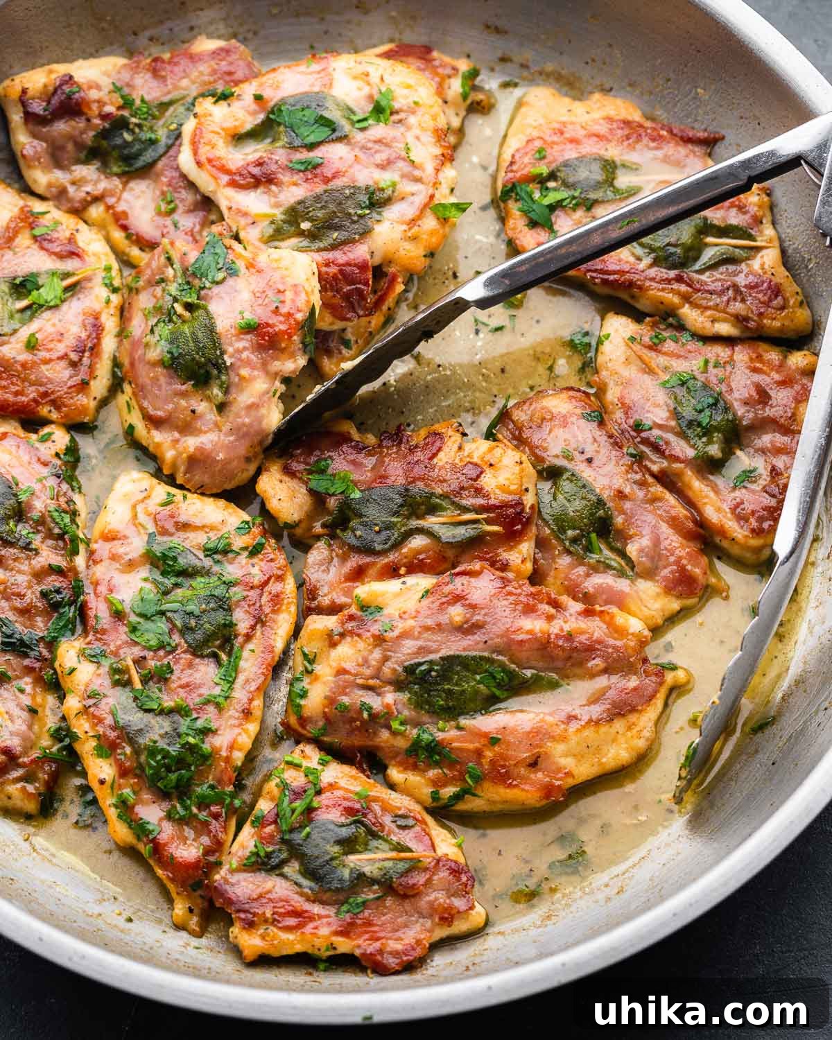 Prosciutto and Sage Chicken Saltimbocca 2 Large pan and tongs with finished chicken saltimbocca, garnished with fresh herbs.