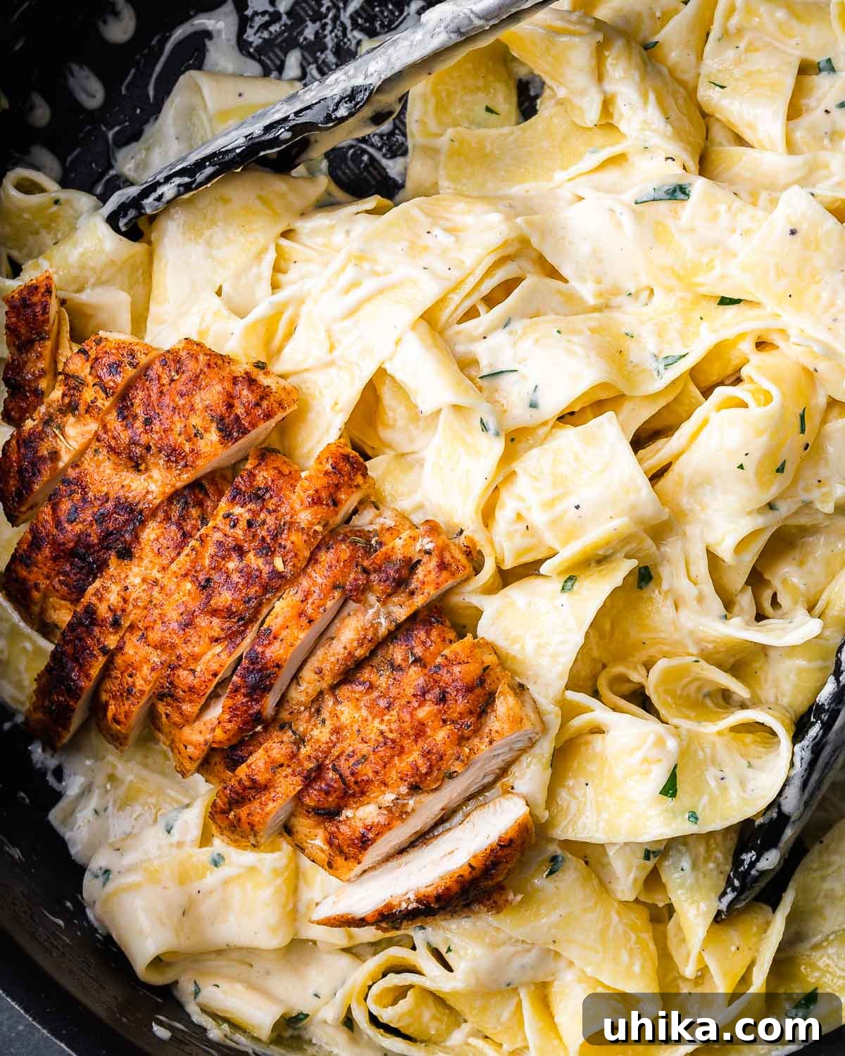 Decadent Chicken Alfredo Pasta 8 Finished chicken alfredo pasta in a black pan with serving tongs.