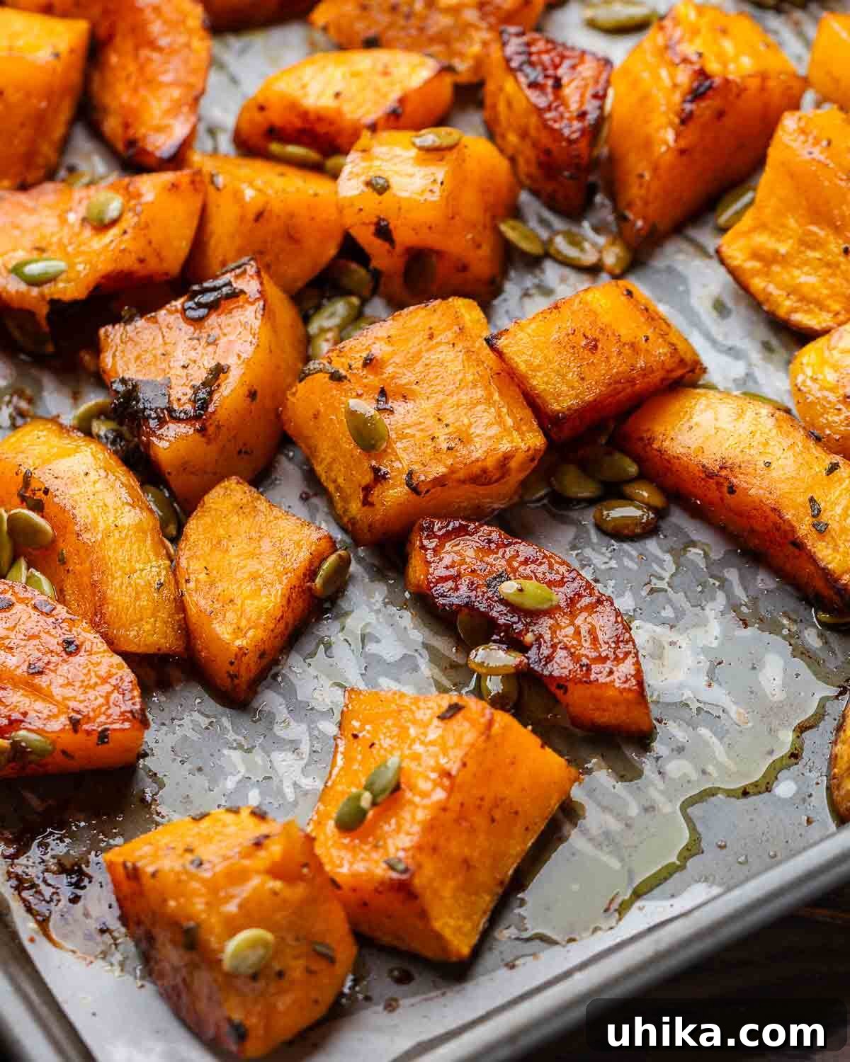 Cinnamon roasted butternut squash on grey baking sheet, garnished with fresh sage leaves and pumpkin seeds.