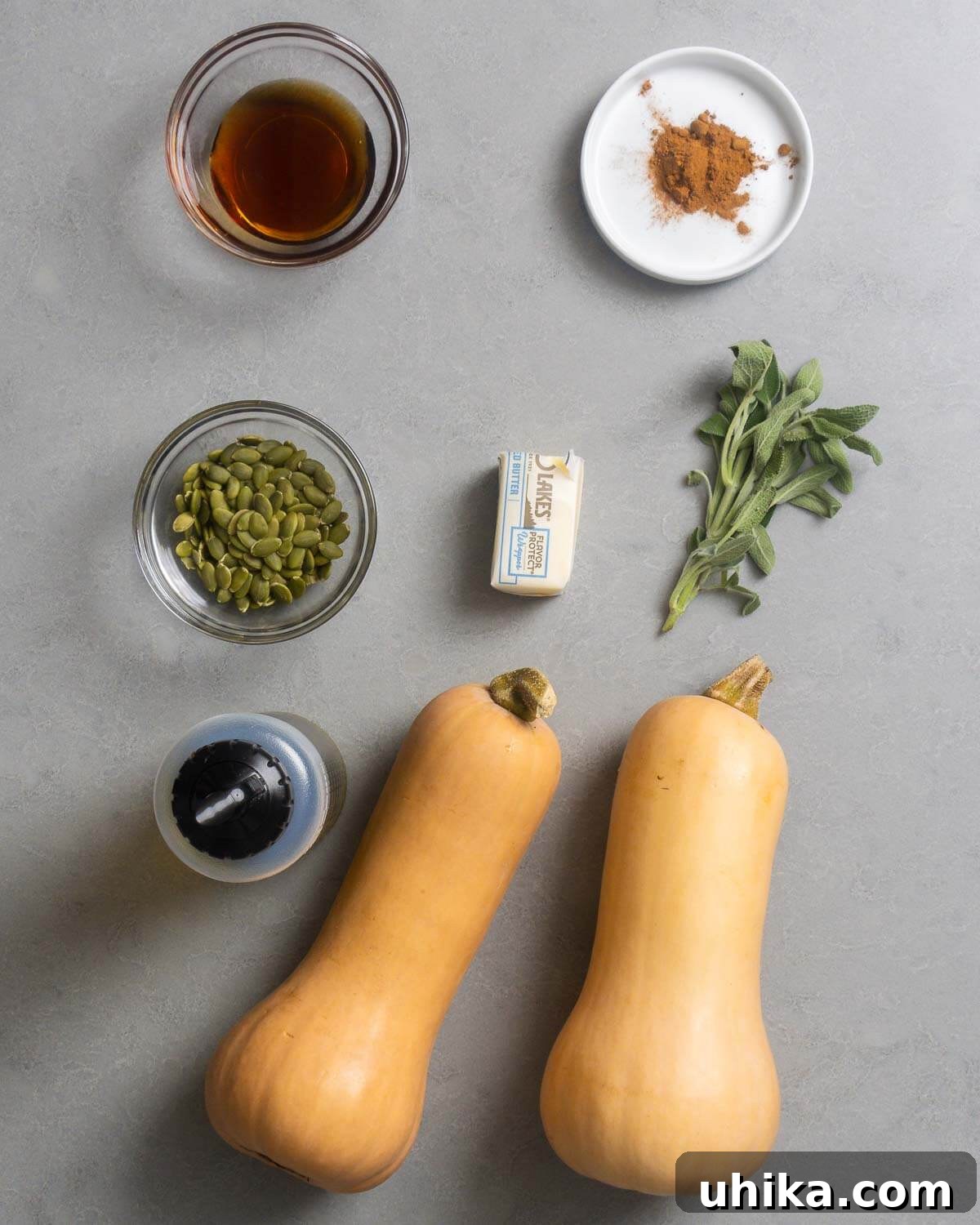 Ingredients for cinnamon roasted butternut squash, including maple syrup, ground cinnamon, pumpkin seeds, butter, fresh sage, olive oil, and raw butternut squash.