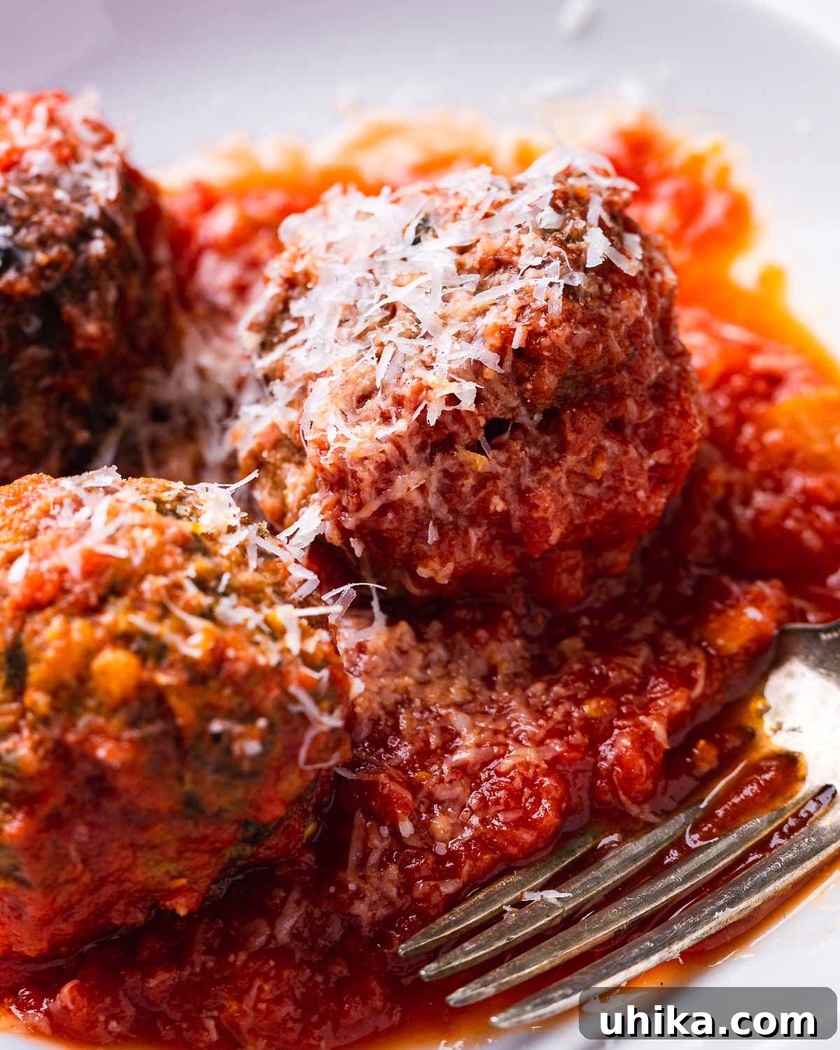 Mama's Sicilian Meatballs 2 Sicilian meatballs in white plate with shaved Pecorino Romano.