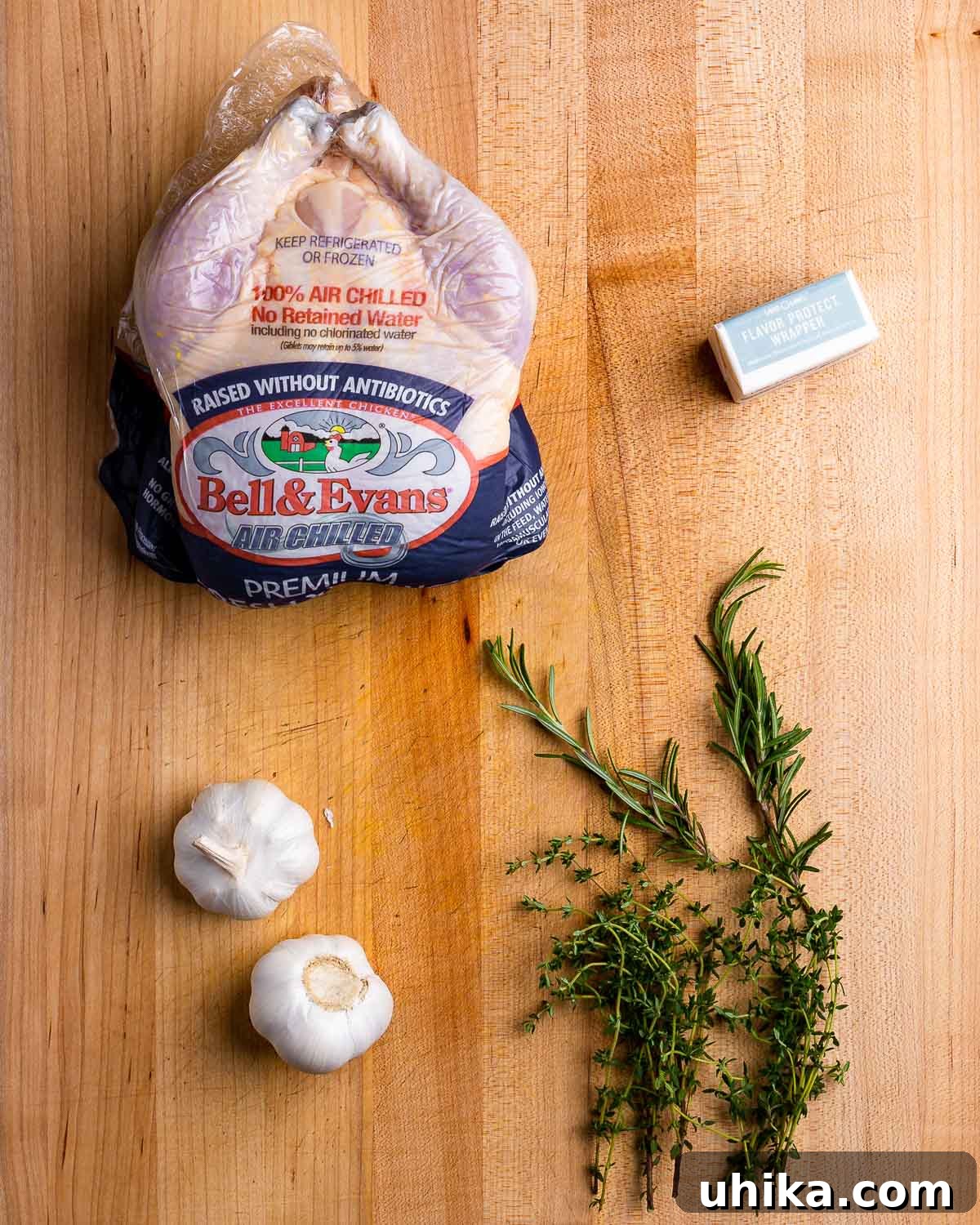 Golden Garlic Butter Roast Chicken 3 Ingredients for garlic butter roast chicken: whole chicken, butter, garlic, fresh rosemary and thyme arranged on a cutting board.