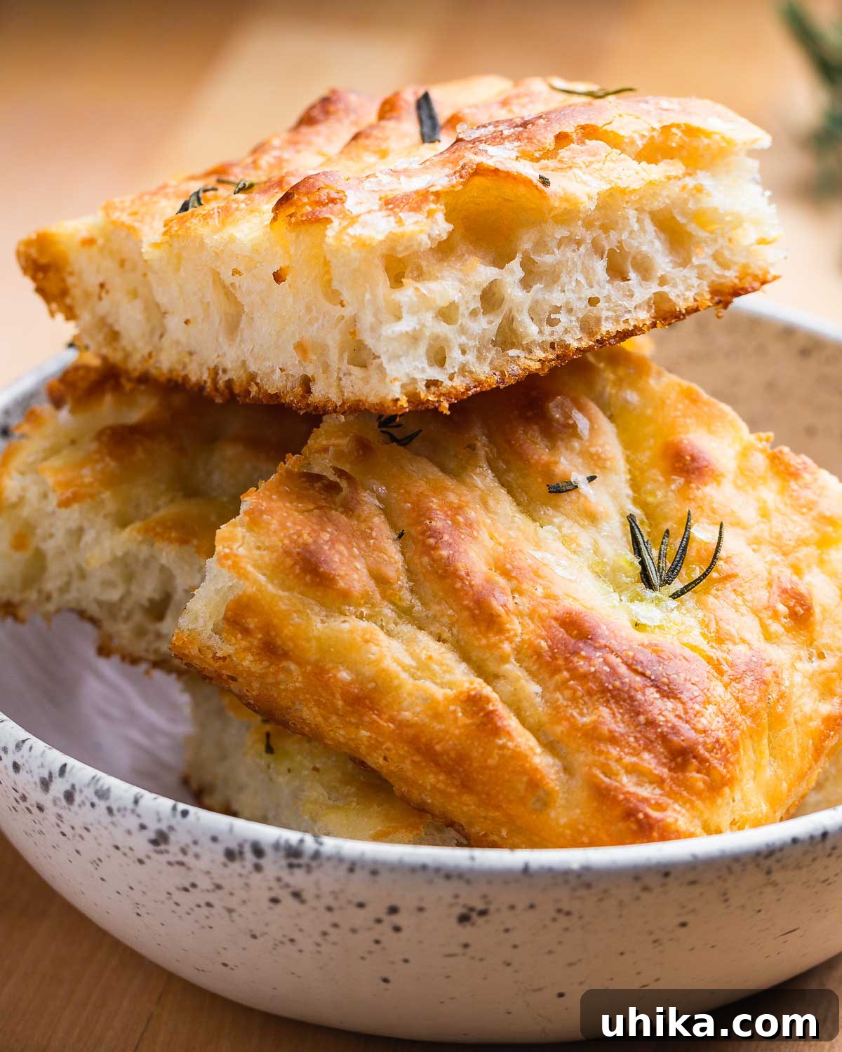 Effortless No-Knead Focaccia 7 A white bowl holds four perfectly baked pieces of golden focaccia, ready to be enjoyed.