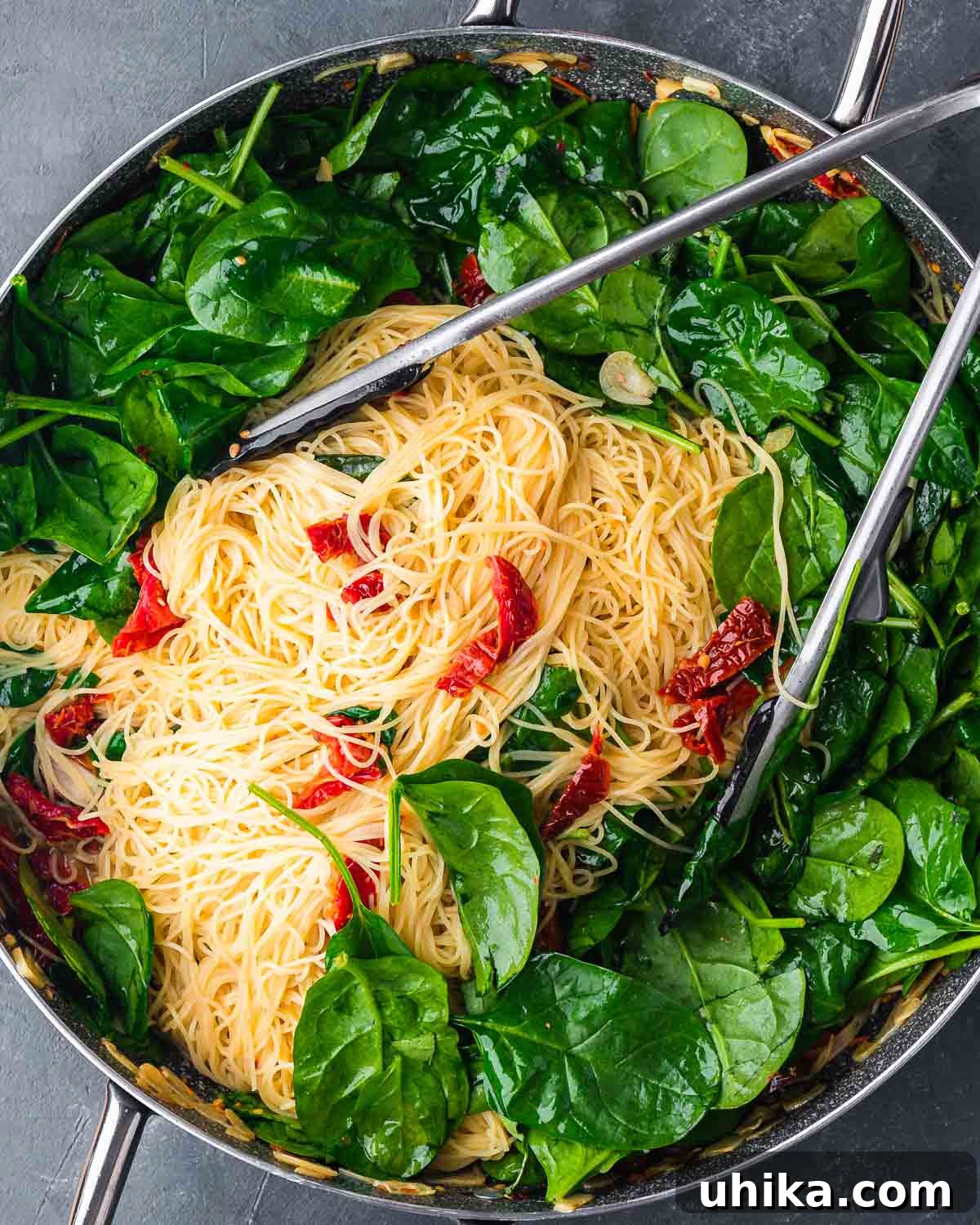 Sun-Drenched Spinach and Tomato Pasta 8 Overhead shot of spinach sun dried tomato pasta in large pan on blue background, showing texture and vibrant colors.