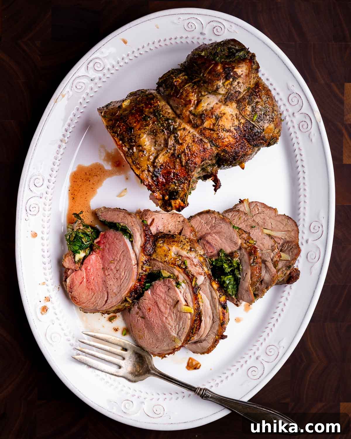 Garlic Rosemary Roasted Lamb Leg 2 Sliced leg of lamb in white platter on brown cutting board.