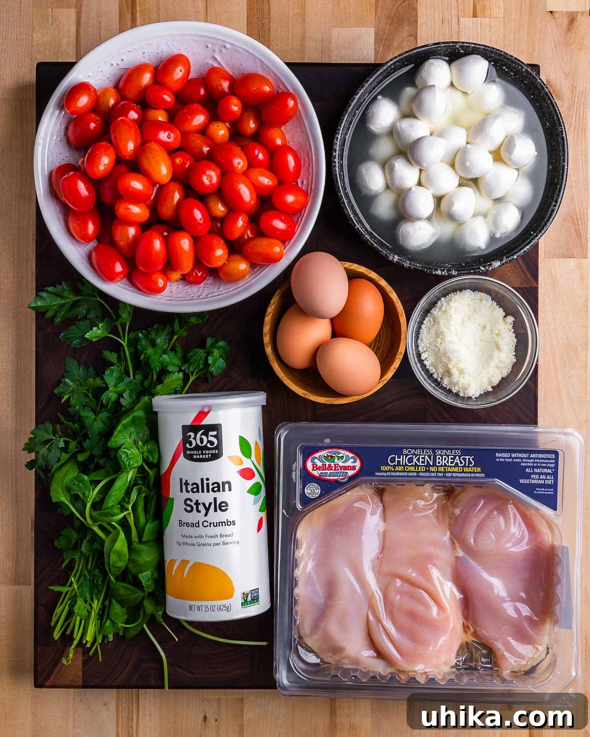 Caprese Chicken Milanese 3 A flat lay photograph showcasing all the fresh ingredients for Chicken Milanese and Caprese salad: vibrant cherry tomatoes, creamy mozzarella balls, fresh parsley, Italian seasoned breadcrumbs, eggs, grated Pecorino Romano cheese, and raw chicken cutlets.