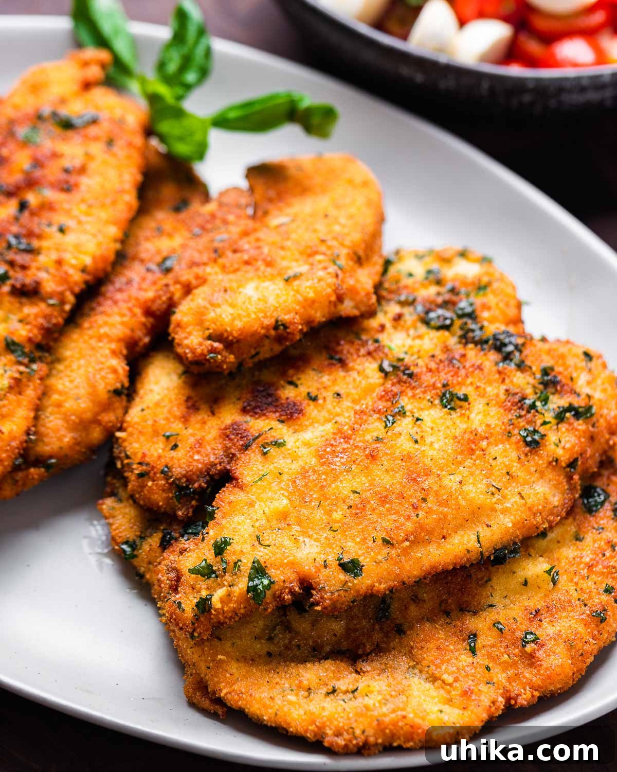 Caprese Chicken Milanese 9 A large platter filled with golden-brown chicken Milanese cutlets, ready to be topped with salad.