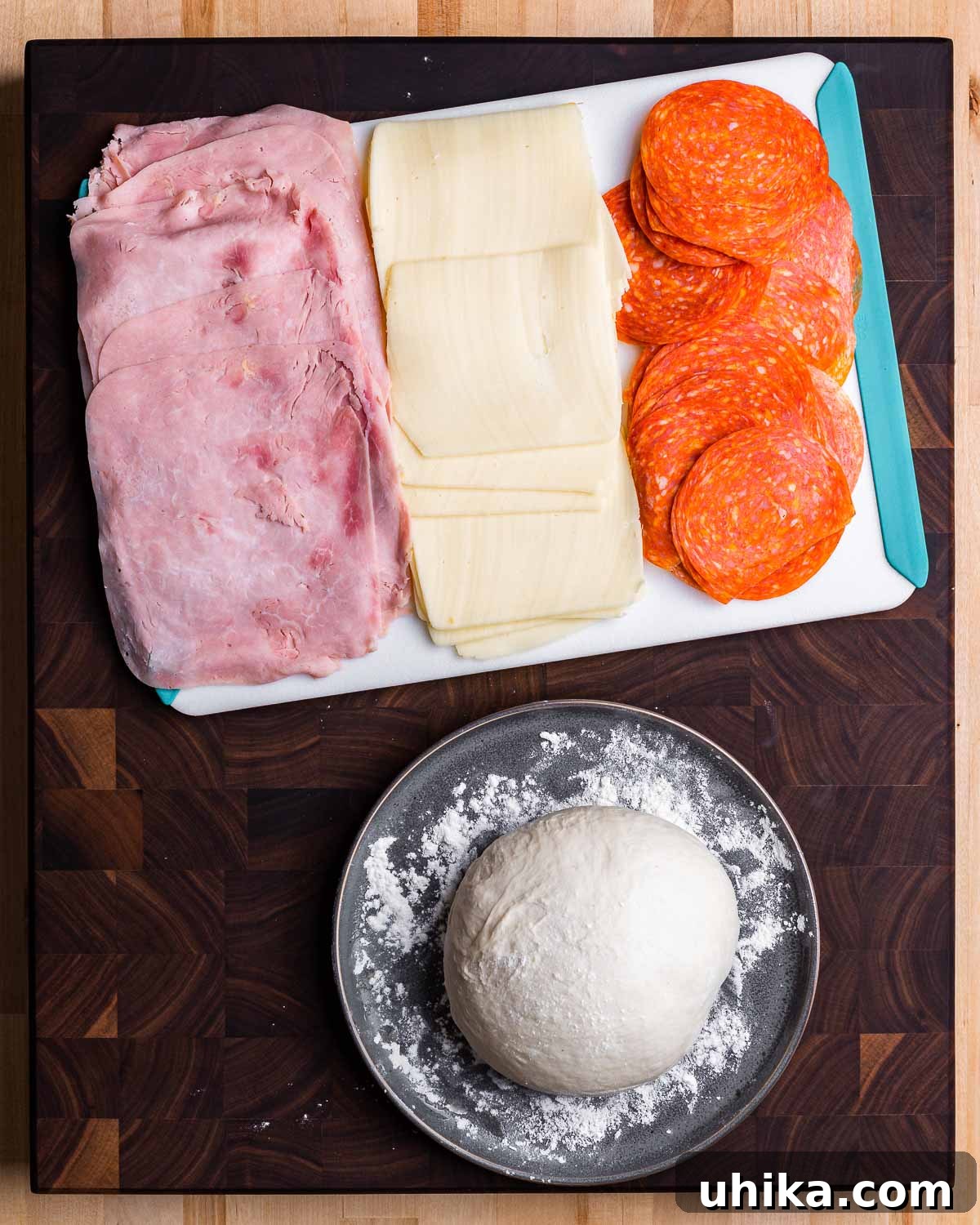 Ingredients for pepperoni pinwheels: cutting board with ham, mozzarella, pepperoni, and a bowl with pizza dough.