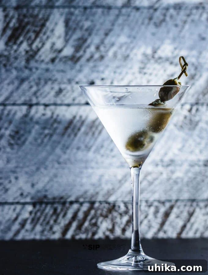 Blue Cheese Olive Martini - sipandfeast.com #martini #cocktails #bluecheese #olives A perfectly chilled gin martini, garnished with three gourmet blue cheese stuffed olives on a skewer, exuding sophistication and flavor.