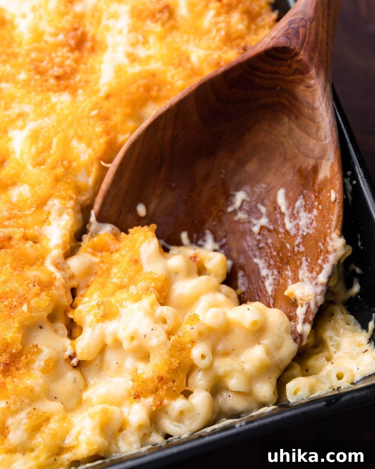 Golden Crusted Creamy Macaroni Bake 4 Large wooden spoon scooping creamy baked mac and cheese from a baking dish.