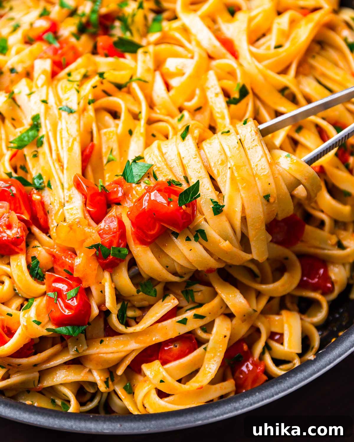 Blushing Cherry Tomato Butter Fettuccine 8 Kitchen tweezers holding a serving of fettuccine with cherry tomato butter sauce in a black pan, ready to be served.