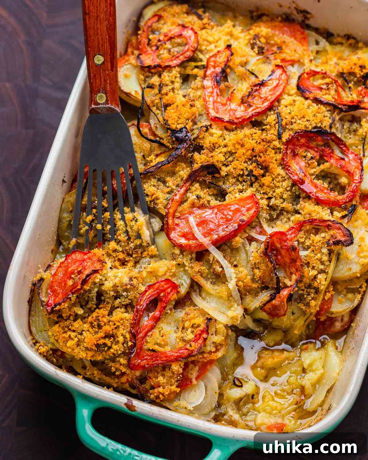 Hearty Italian Potato Gratin 8 A serving of Italian potato casserole being lifted from the baking dish with a spatula, set on a wooden cutting board.