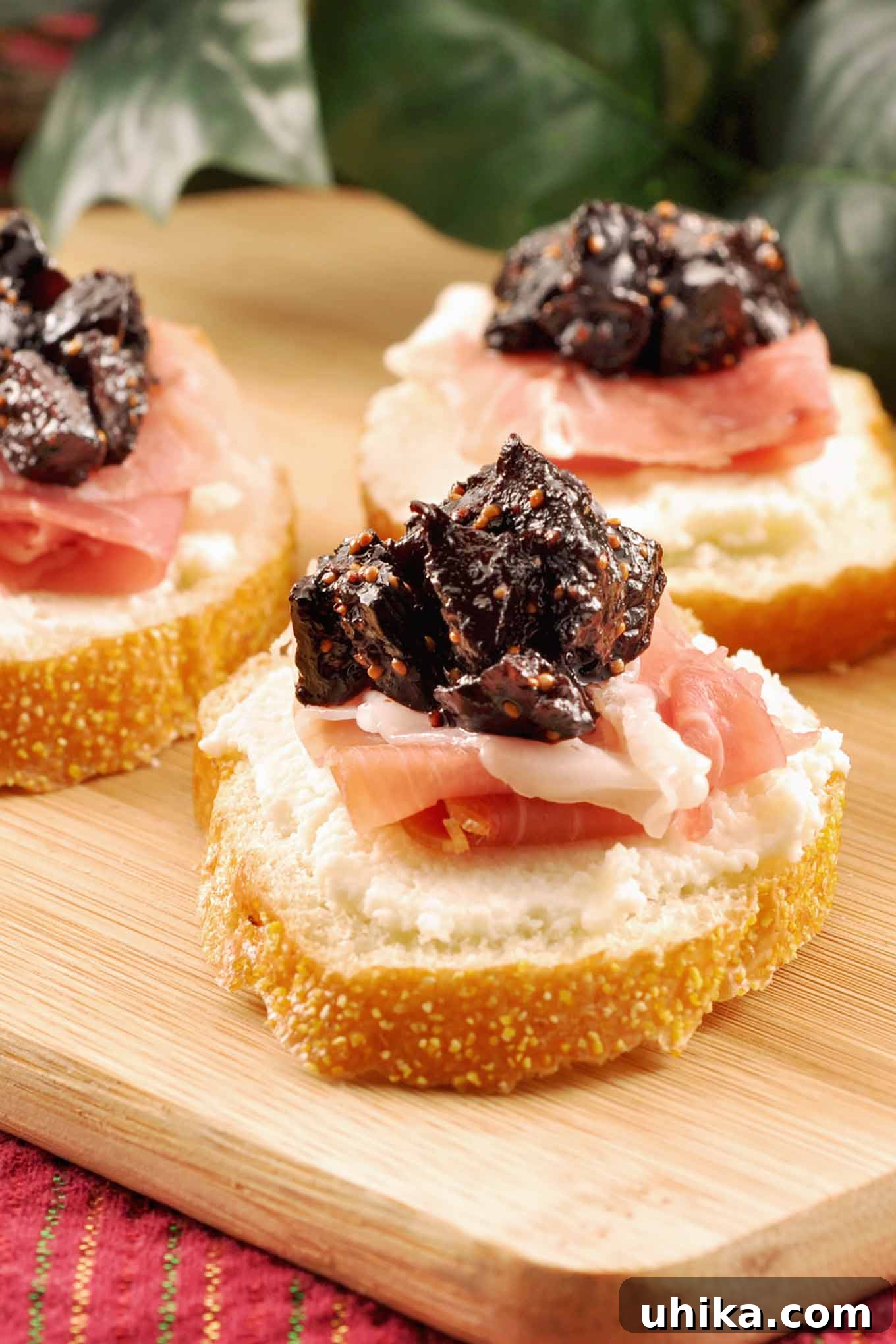 Three crostini topped with whipped ricotta, prosciutto, and port wine fig compote arranged on a wooden cutting board.