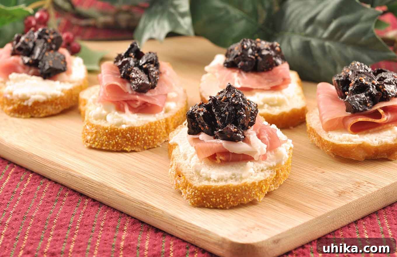 Crostini topped with whipped ricotta, prosciutto, and port wine fig compote on a cutting board with Christmas table decor in the background.