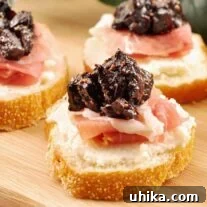 Three crostini topped with whipped ricotta, prosciutto, and port wine fig compote arranged on a wooden cutting board.