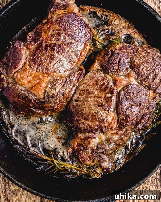 Reverse Seared Ribeye Steaks - sipandfeast.com #reversesear #ribeye #steak #dinner Picture of ribeyes in cast iron pan with rosemary.