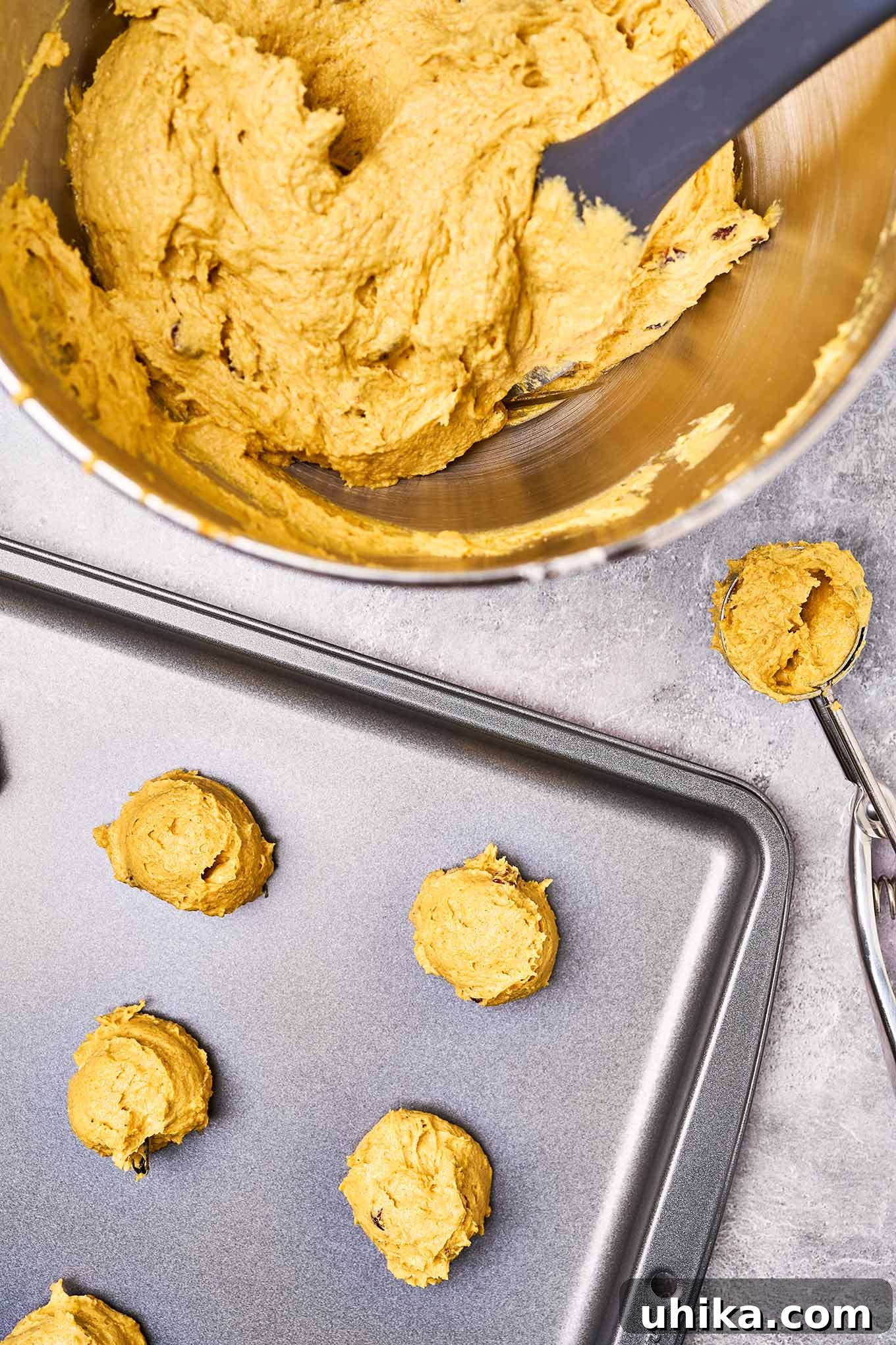 Spiced Pumpkin Cranberry Cookie Delights 5 An overhead view of a cookie sheet with pumpkin cookies ready for baking, a cookie scoop, and dough in a mixing bowl.