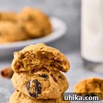A stack of three soft pumpkin cookies with dried cranberries, one with a bite removed, milk, and more cookies in the background.