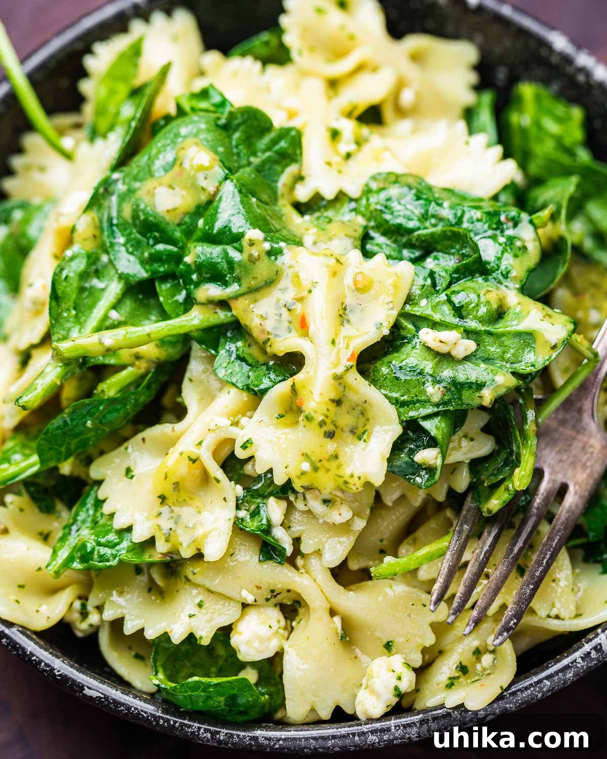 Creamy Gorgonzola & Spinach Pasta Salad 2 A dark bowl brimming with fresh Spinach Gorgonzola Pasta Salad, featuring green spinach, white pasta, and blue cheese crumbles.