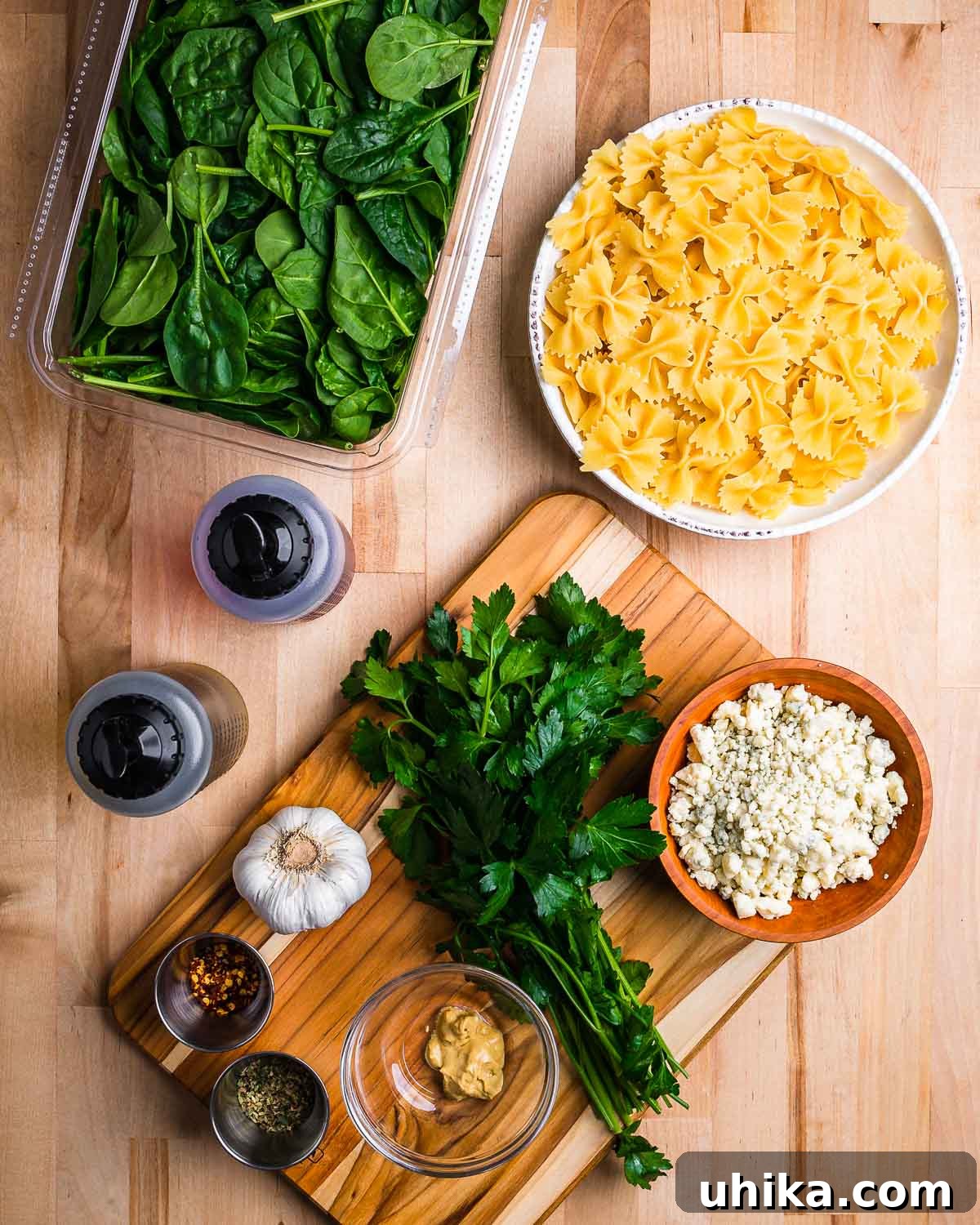 Creamy Gorgonzola & Spinach Pasta Salad 3 A flat lay of all ingredients for Spinach Gorgonzola Pasta Salad: baby spinach, bow tie pasta, olive oil, red wine vinegar, crumbled gorgonzola, fresh parsley, minced garlic, Dijon mustard, red pepper flakes, and dried oregano.
