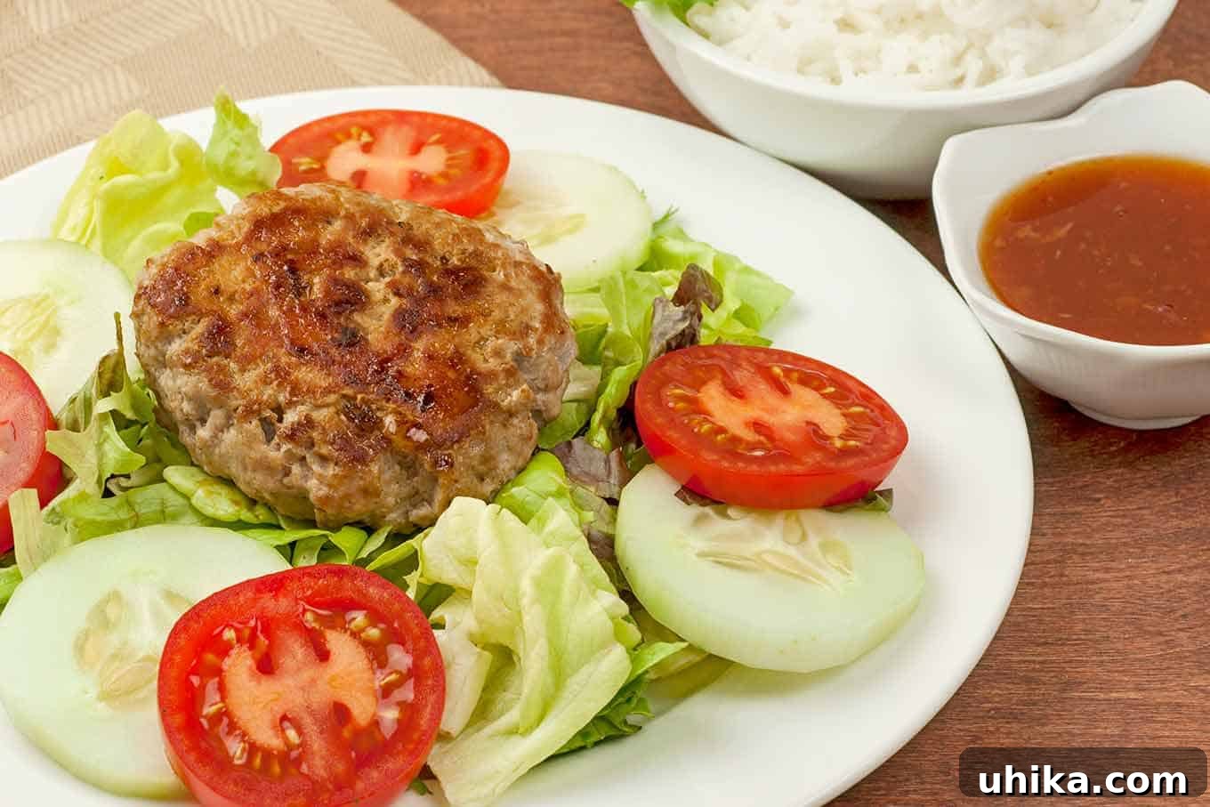 Savory Vietnamese Pork Patties with Zesty Dipping Sauce 3 A beautifully arranged plate featuring a Vietnamese pork patty atop fresh lettuce, flanked by sliced tomatoes and cucumbers, with a side of white rice and tangy dipping sauce.