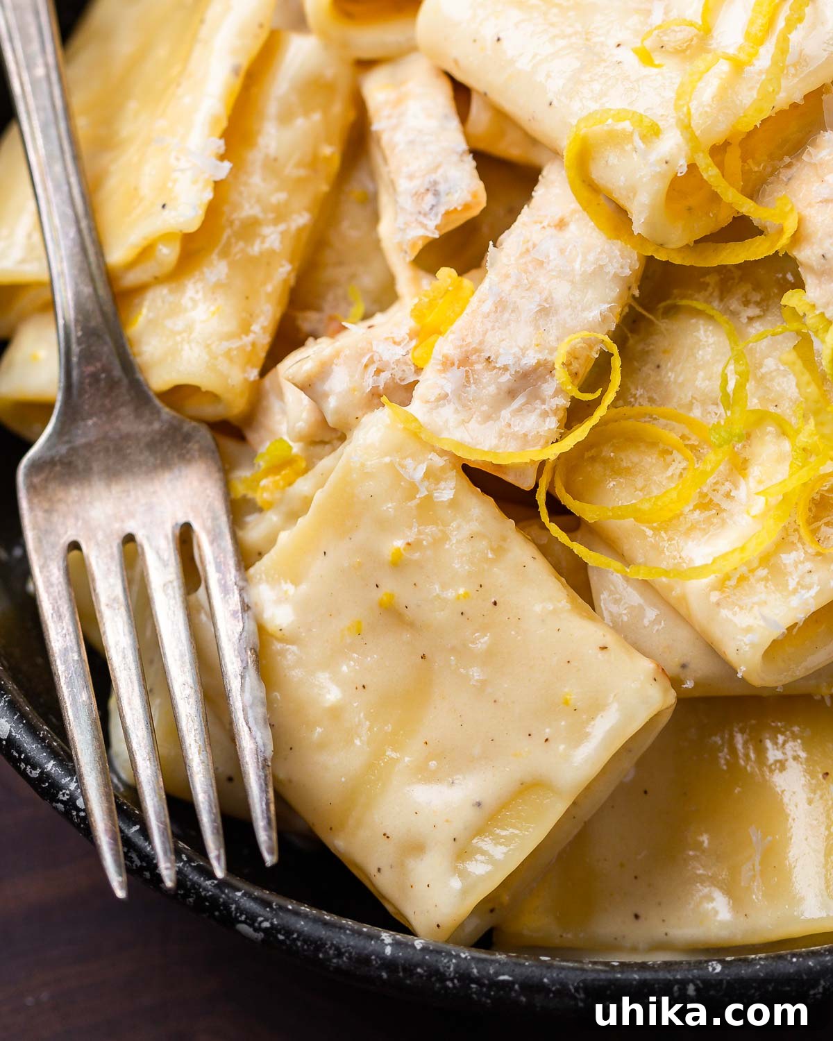 Luscious Lemon Chicken Pasta 2 Creamy lemon chicken pasta in black bowl with lemon zest and cheese on top.