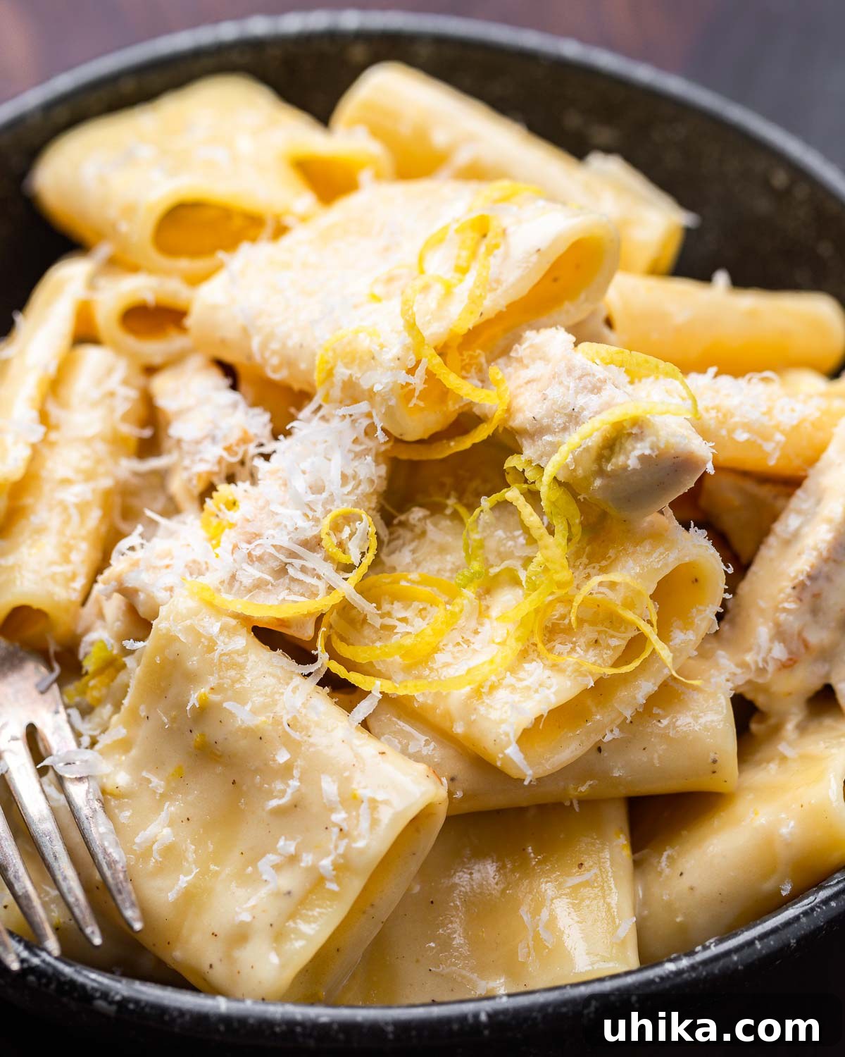 Luscious Lemon Chicken Pasta 7 Creamy lemon chicken pasta in black bowl with lemon zest and cheese on top.