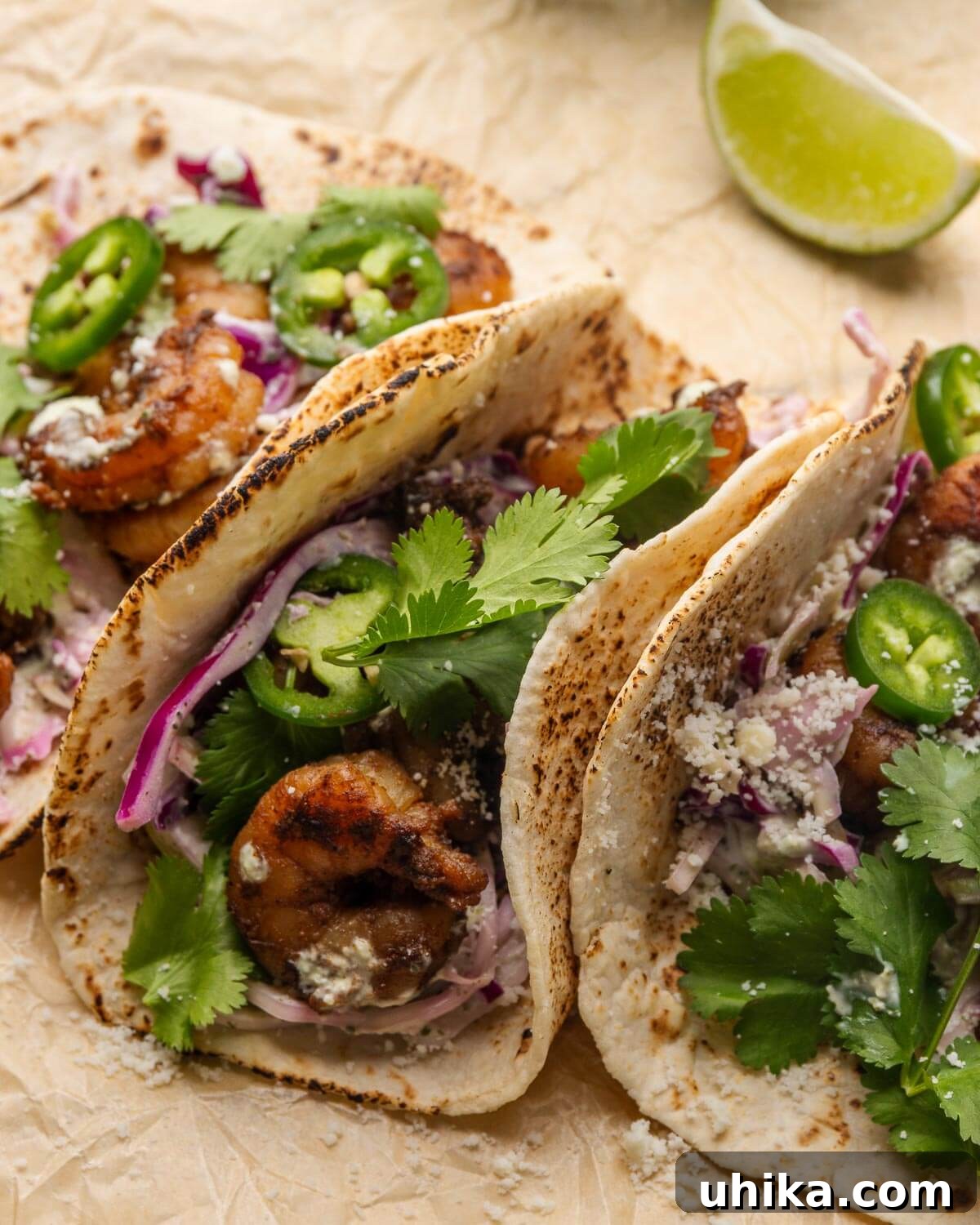 Fiery Shrimp Tacos with Cool Cilantro Jalapeno Crema 2 Vibrant spicy shrimp tacos garnished with fresh cilantro and lime wedges, presented on rustic brown parchment paper.