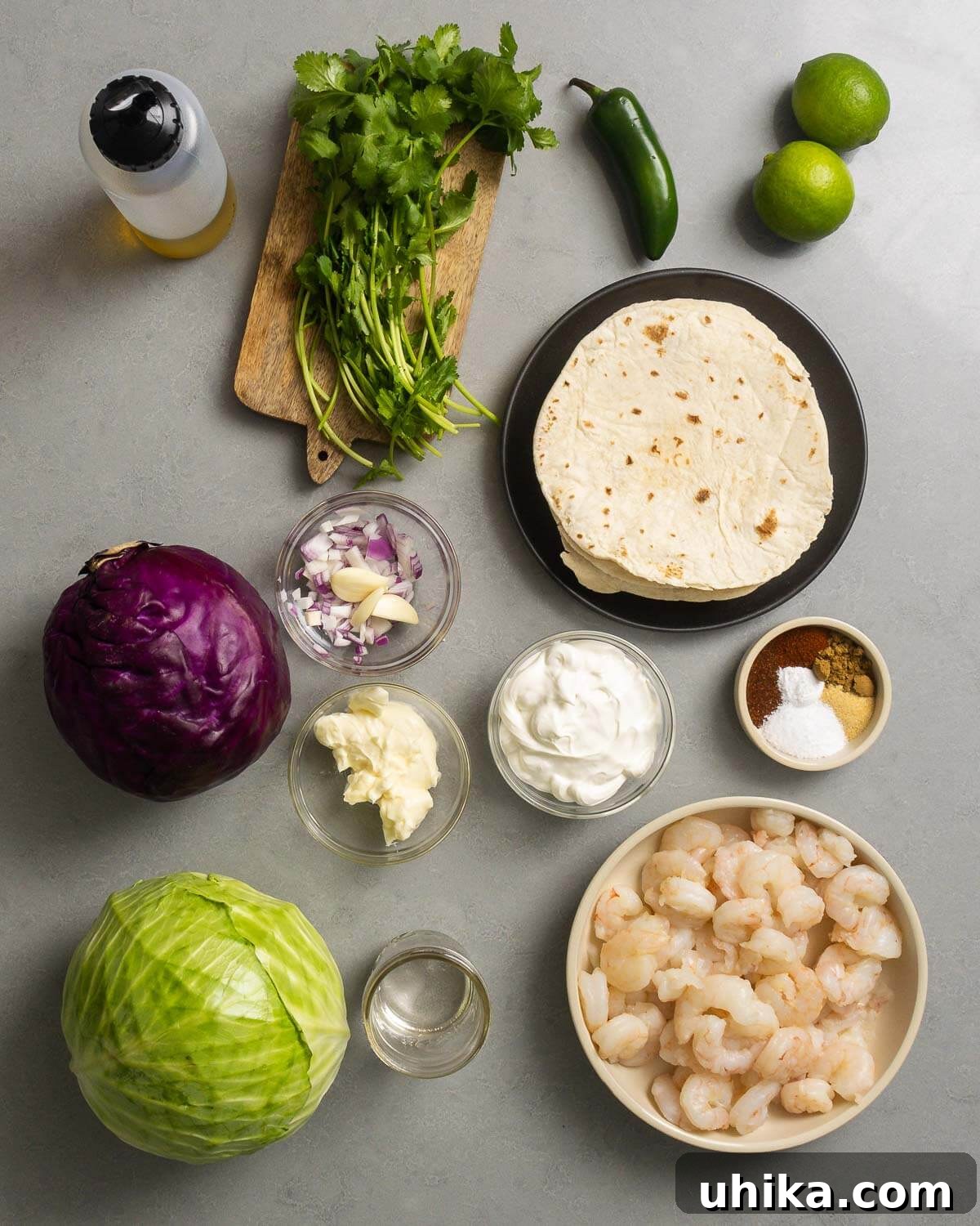 Fiery Shrimp Tacos with Cool Cilantro Jalapeno Crema 3 A colorful array of ingredients for spicy shrimp tacos: olive oil, fresh cilantro, vibrant jalapeños, limes, tortillas, garlic, onion, shredded cabbage, creamy mayonnaise, sour cream, a blend of spices and chili powder, a bottle of tequila, and fresh shrimp.