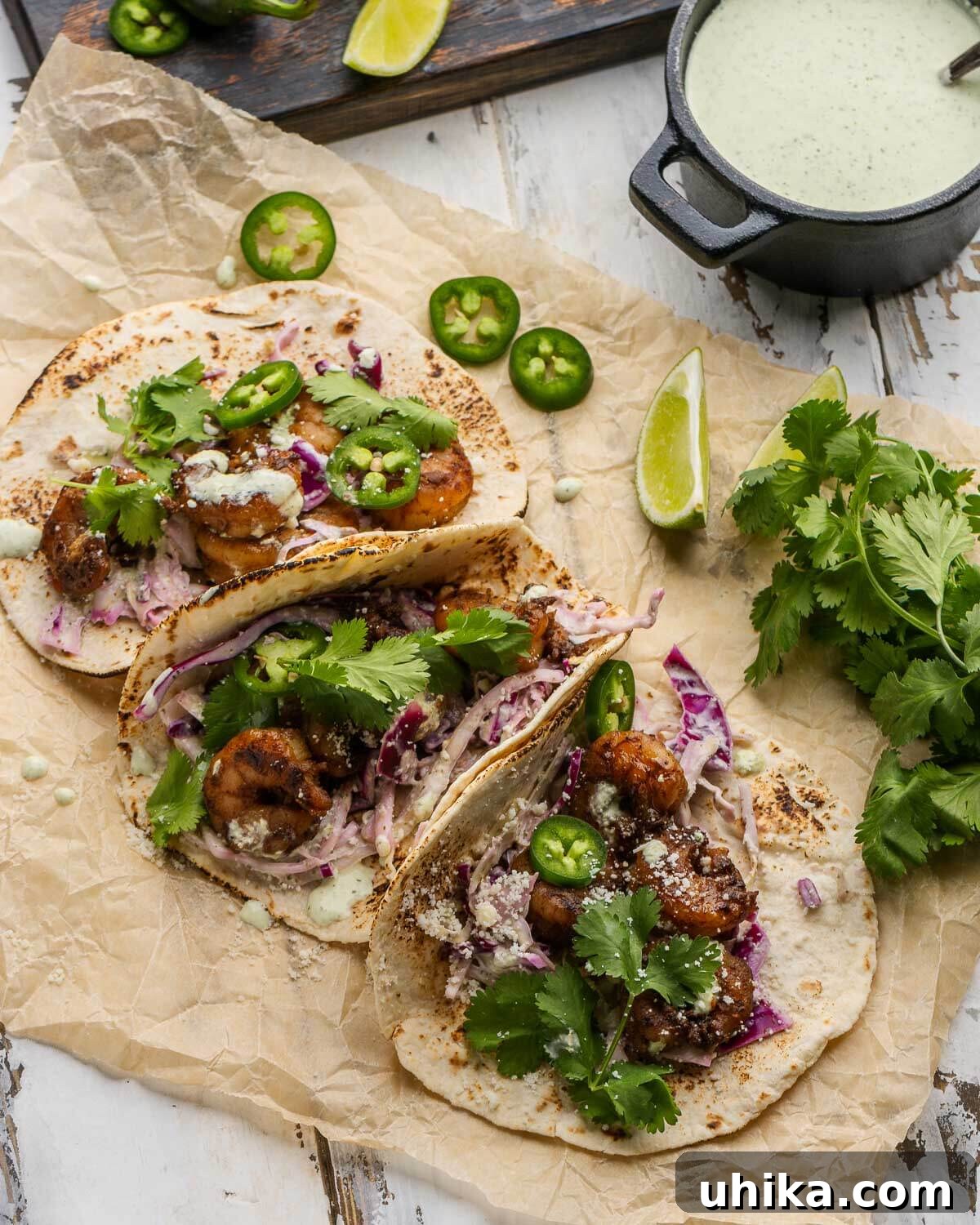 Fiery Shrimp Tacos with Cool Cilantro Jalapeno Crema 6 Three perfectly assembled spicy shrimp tacos on parchment paper, adorned with fresh jalapeños, lime wedges, and cilantro, alongside a black bowl of creamy jalapeño sauce for extra drizzling.