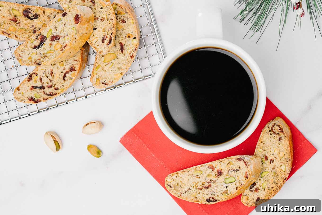 Jeweled Cranberry Pistachio Biscotti 3 An overhead view of a cranberry pistachio biscotti on a cooling rack next to a cup of coffee and two biscotti on a red napkin.