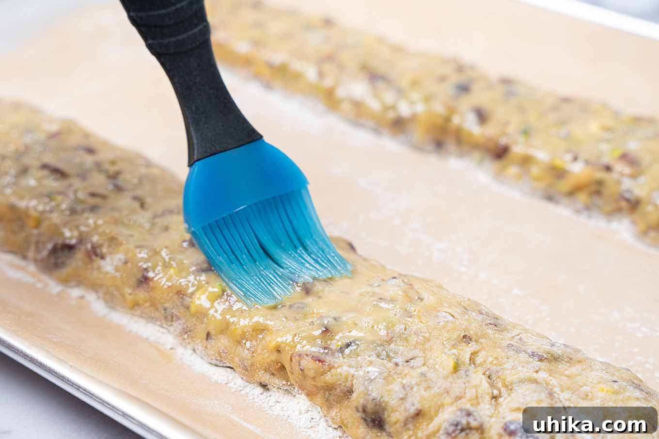 Jeweled Cranberry Pistachio Biscotti 4 Cranberry pistachio biscotti dough on a baking sheet, being brushed with beaten egg prior to first baking.