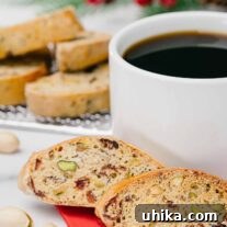Cranberry pistachio biscotti in front of a cup of coffee, with more biscotti on a cooling rack in the background.