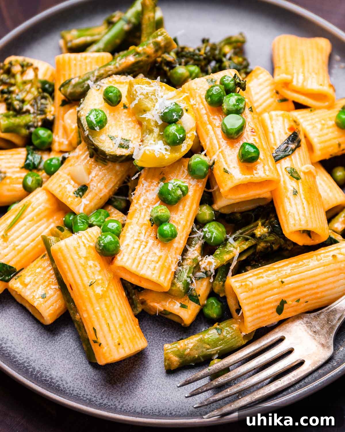 Spring Garden Rigatoni 2 A vibrant dish of Rigatoni Primavera served in a stylish grey plate, accompanied by a fork, highlighting the colorful vegetables and creamy sauce.