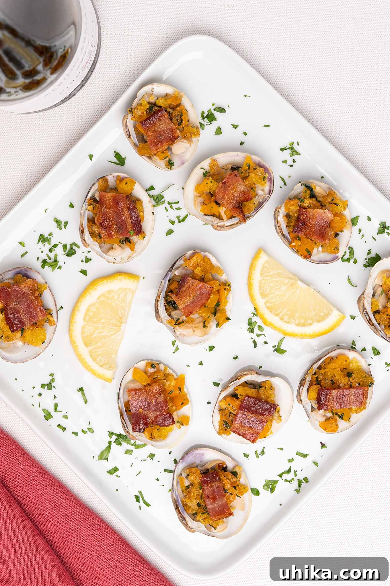 Clams Casino topped with crispy bacon and arranged on an elegant appetizer serving plate with fresh lemon wedges and vibrant parsley garnish, ready to be enjoyed.