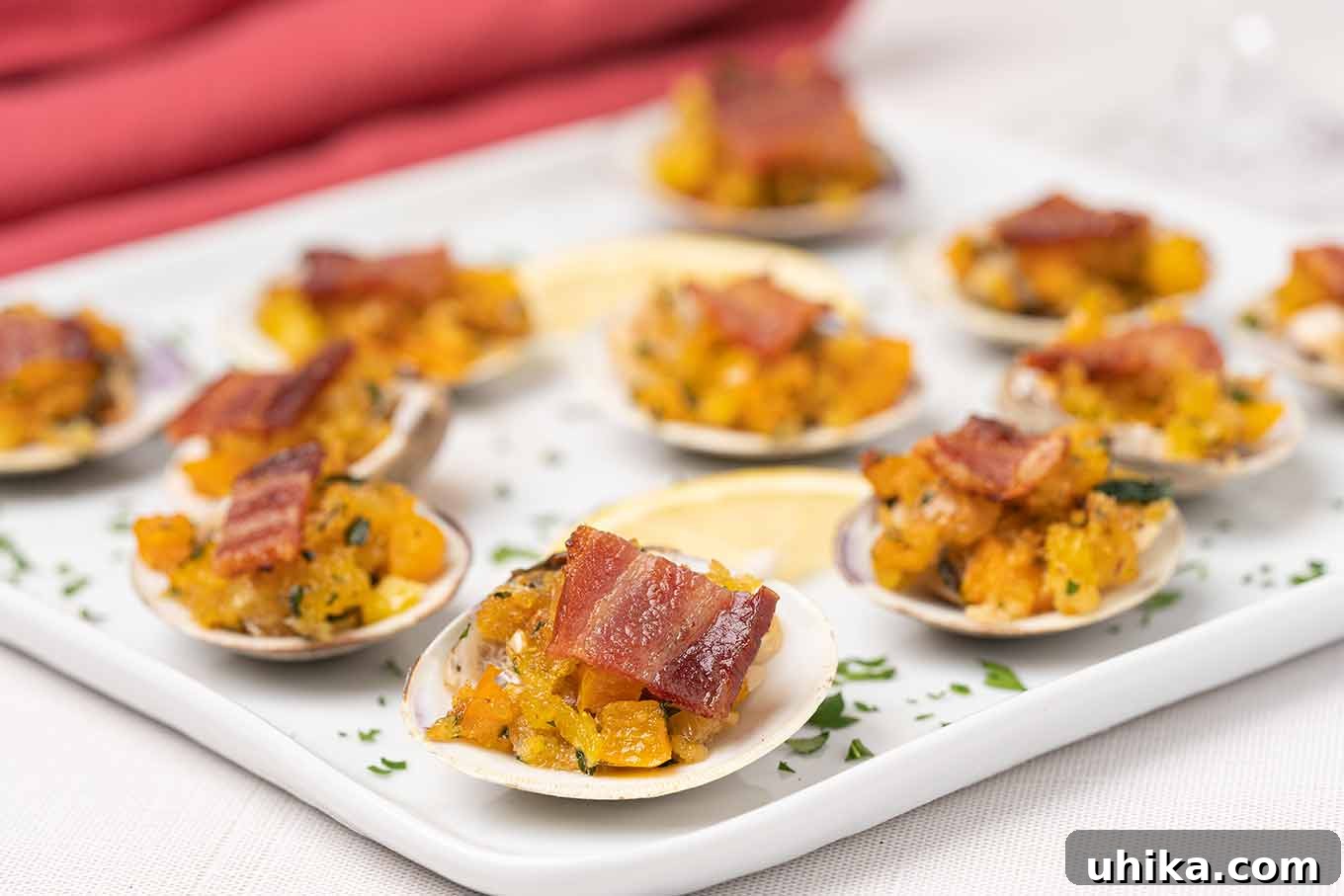 Classic New England Clams Casino dish arranged on a pristine white serving plate, adorned with crispy bacon, fresh parsley, and bright lemon wedges for garnish.