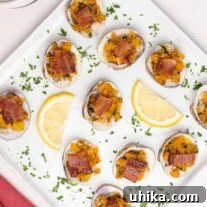 Clams Casino topped with bacon and arranged on an appetizer serving plate with lemon wedges and parsley garnish.