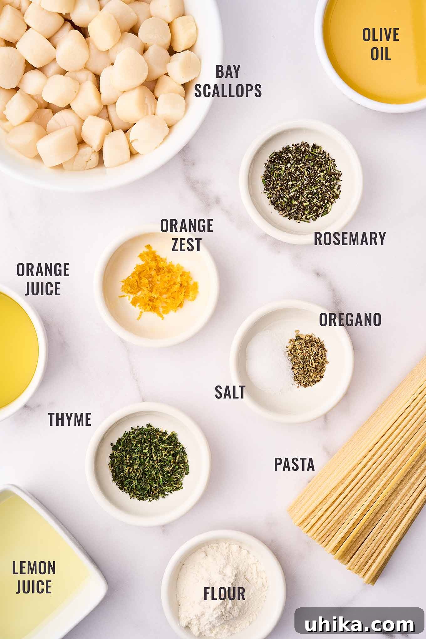 Sun-Kissed Sicilian Bay Scallop Pasta 3 A labeled, overhead view of the ingredients for bay scallop pasta with citrus sauce, including fresh bay scallops, orange juice and zest, lemon juice, garlic, rosemary, oregano, thyme, olive oil, and thin spaghetti.