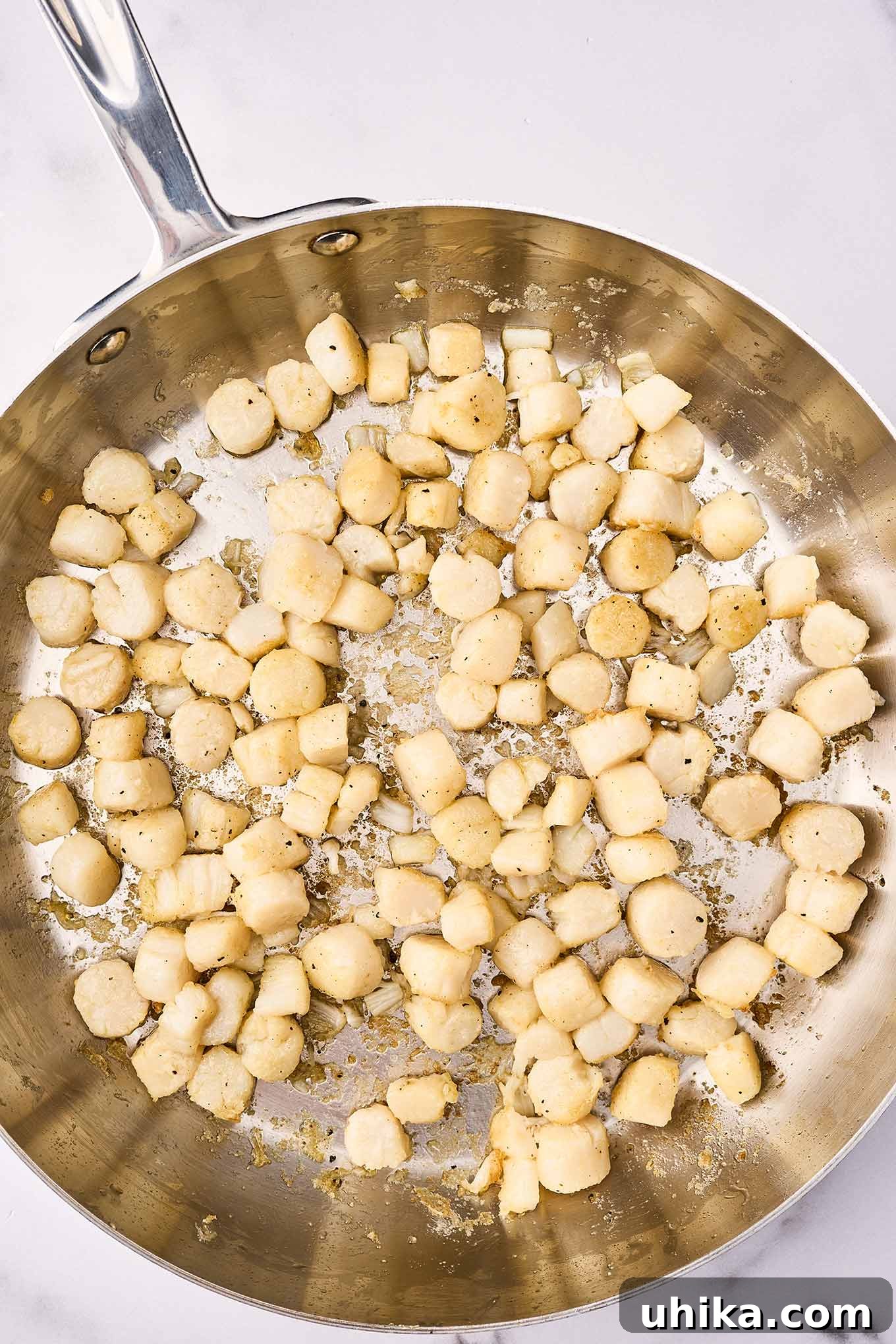 Sun-Kissed Sicilian Bay Scallop Pasta 5 A frying pan with bay scallops being briefly sautéed in olive oil with garlic, ensuring they are tender and perfectly cooked.