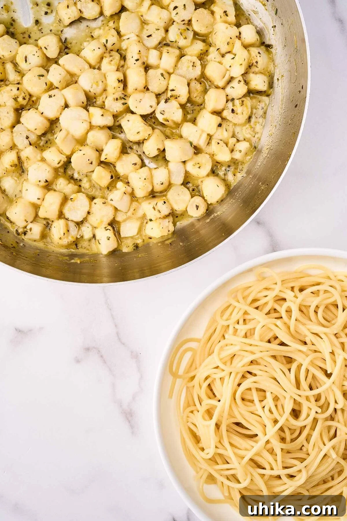 Sun-Kissed Sicilian Bay Scallop Pasta 7 A frying pan with sautéed bay scallops in citrus, herb, and olive oil sauce, positioned next to a bowl of perfectly cooked thin spaghetti, ready to be combined for a delicious meal.