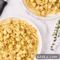 Two servings of bay scallop pasta with Sicilian citrus sauce in shallow white bowls, surrounded by a sprig of fresh thyme, and a citrus zester.