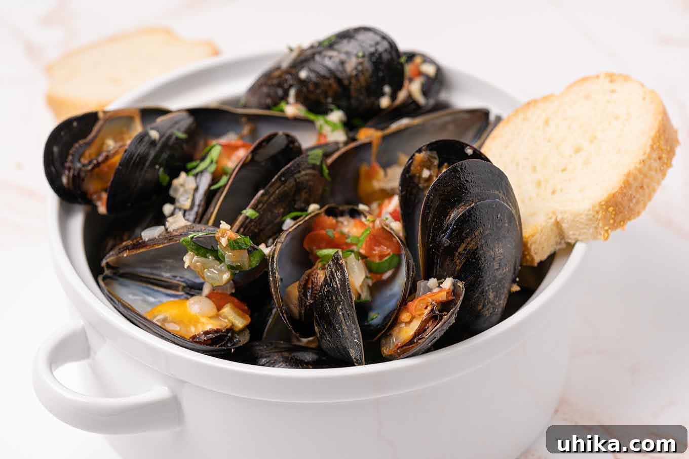 Italian Riviera Mussels 4 A serving bowl filled with steamed mussels topped with bits of garlic, onion, tomato, and parsley and crusty bread for dipping.