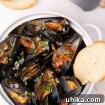 Crock filled with steamed mussels topped with sautéed onion, garlic, diced tomatoes, and parsley.